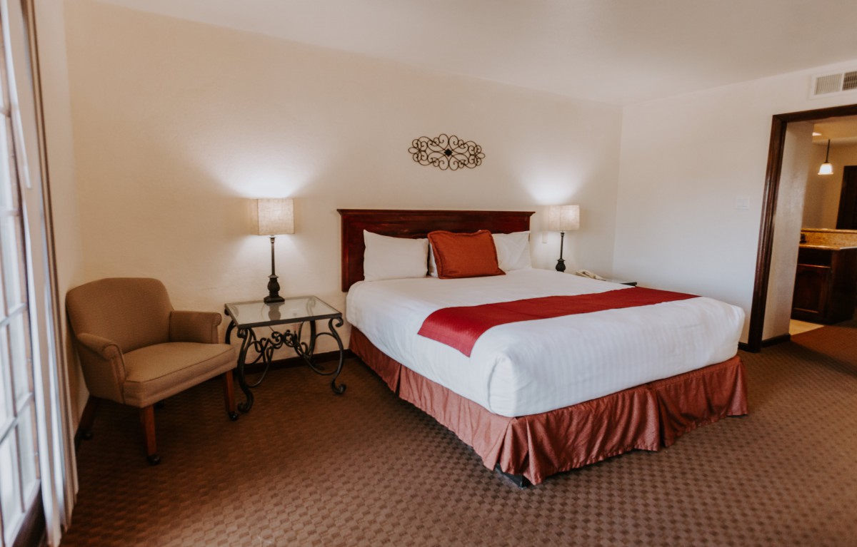A cozy hotel room with a large bed, two lamps on nightstands, and a comfortable chair.