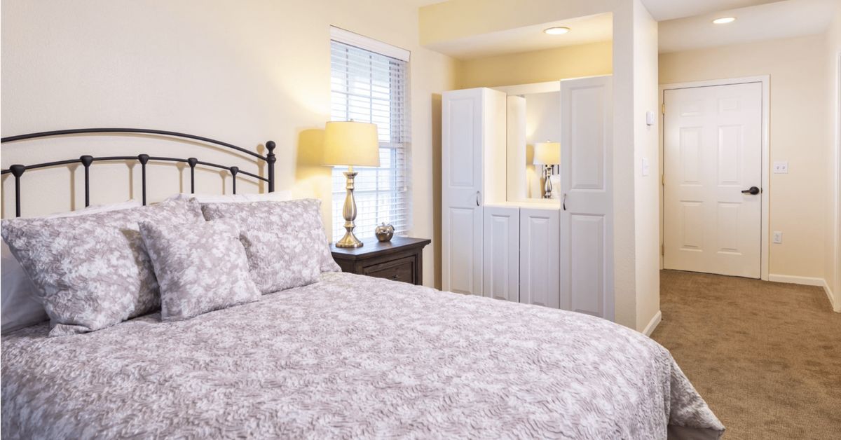 A cozy bedroom with a neatly made bed, bedside lamp, and wardrobe.