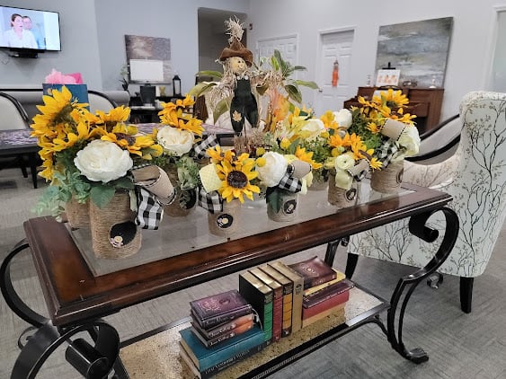 A beautifully decorated table with autumn-themed floral arrangements featuring sunflowers, complemented by a stack of books underneath.
