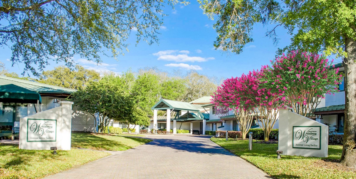 A luxurious mansion surrounded by lush greenery and vibrant trees under a clear blue sky.