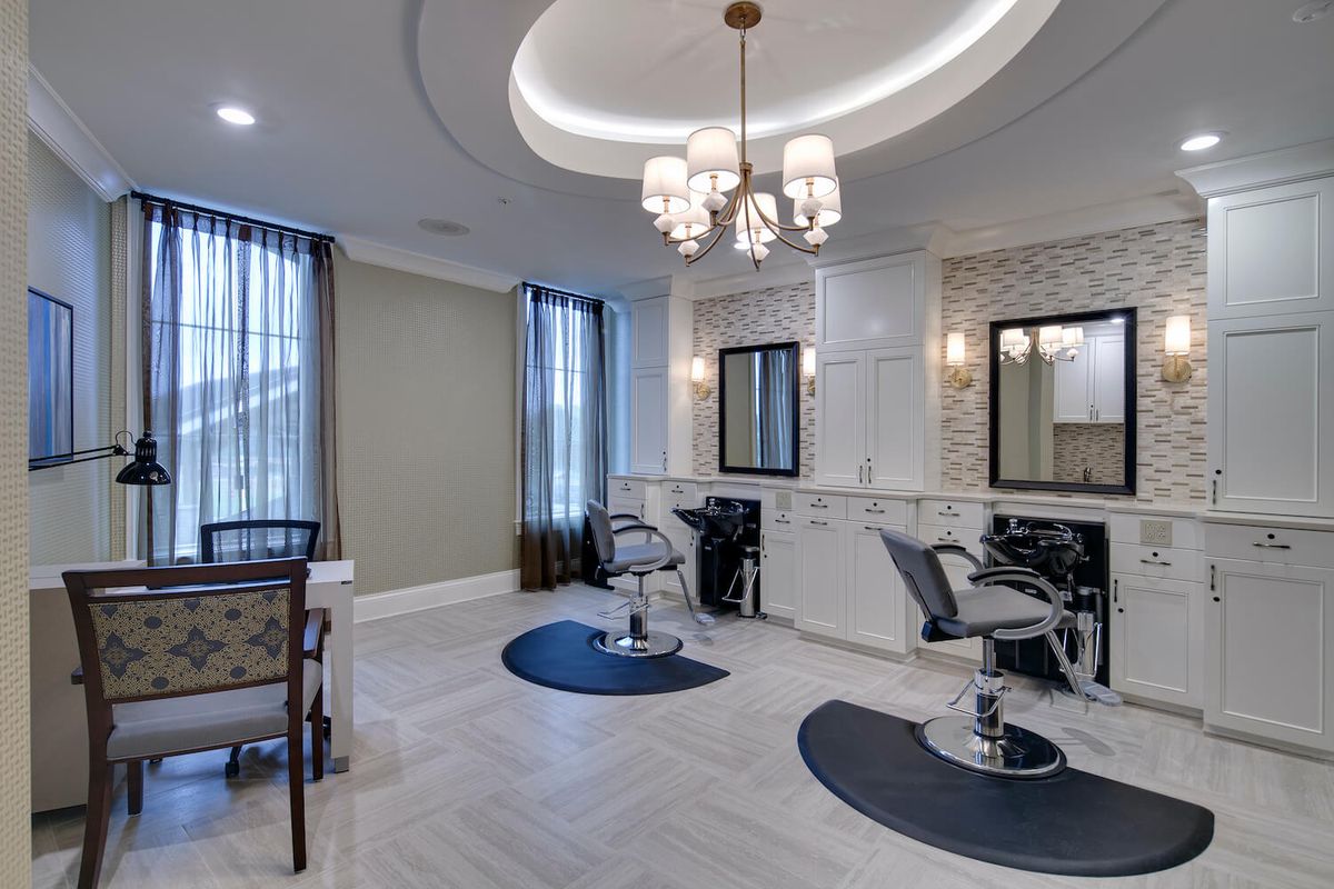An elegant hair salon interior with chandeliers, mirrors, and styling chairs.