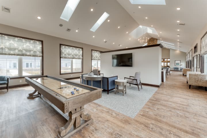 A modern game room featuring a shuffleboard table, skylights, and a mounted television.