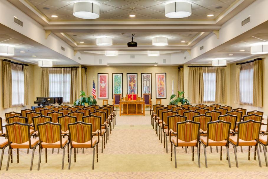 A well-lit conference room with rows of chairs facing a stage adorned with decorative art pieces.