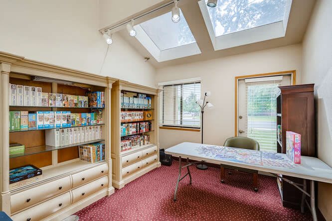 A cozy library room with bookshelves, a table, and skylights for natural lighting.