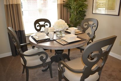 A stylish dining room with a round table set for four, adorned with elegant place settings and a centerpiece of white flowers.