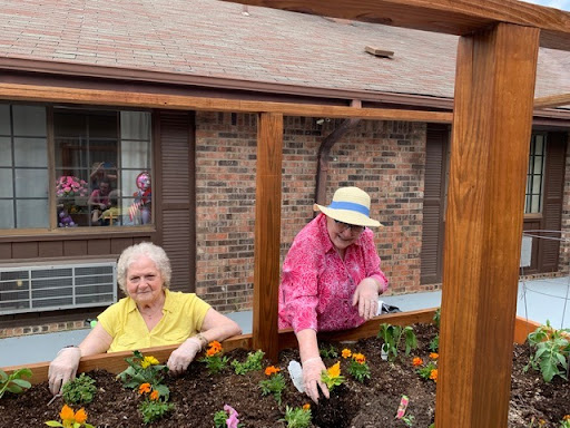 Two elderly women enjoying a sunny day planting flowers in a garden box.