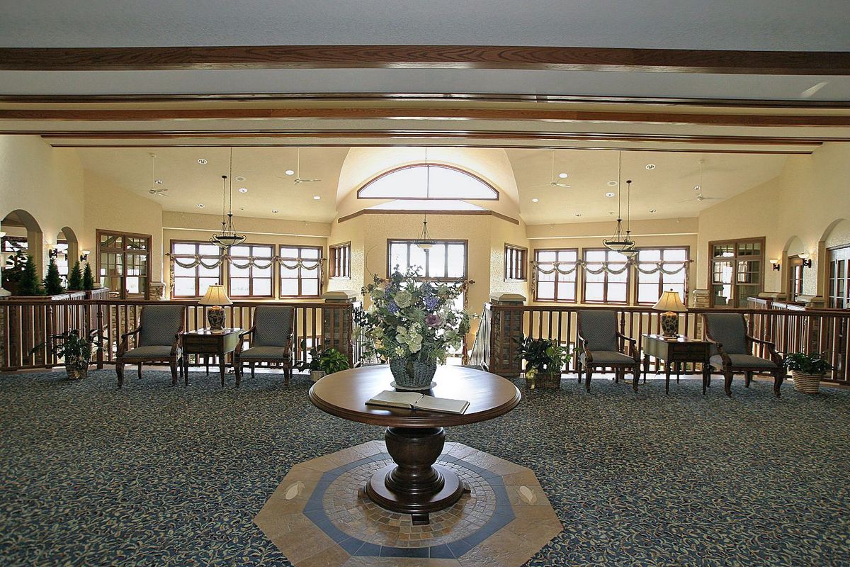 A well-lit lobby area featuring a central table adorned with flowers, surrounded by chairs and large windows.