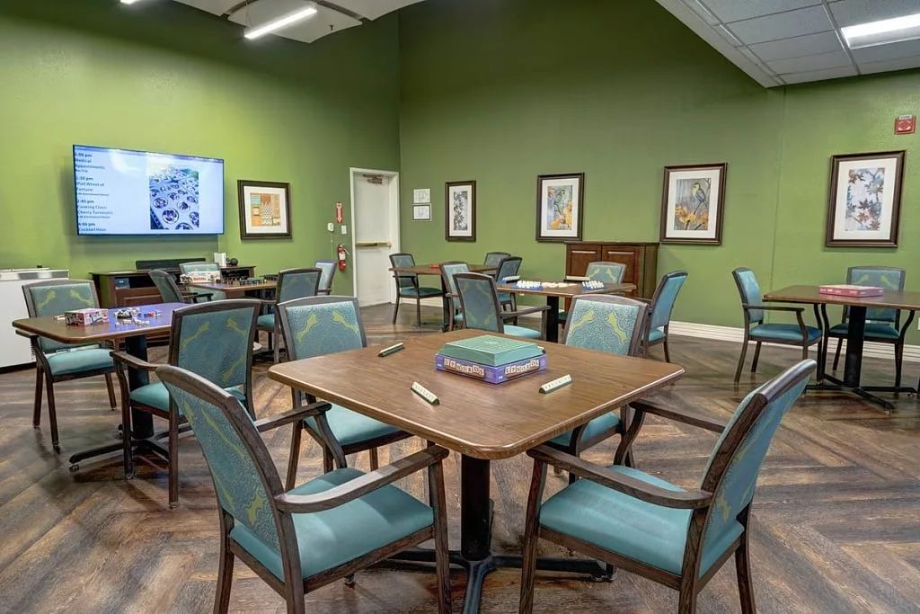 A well-appointed meeting room with green walls, featuring several tables and chairs, a television, and framed artwork on the walls.