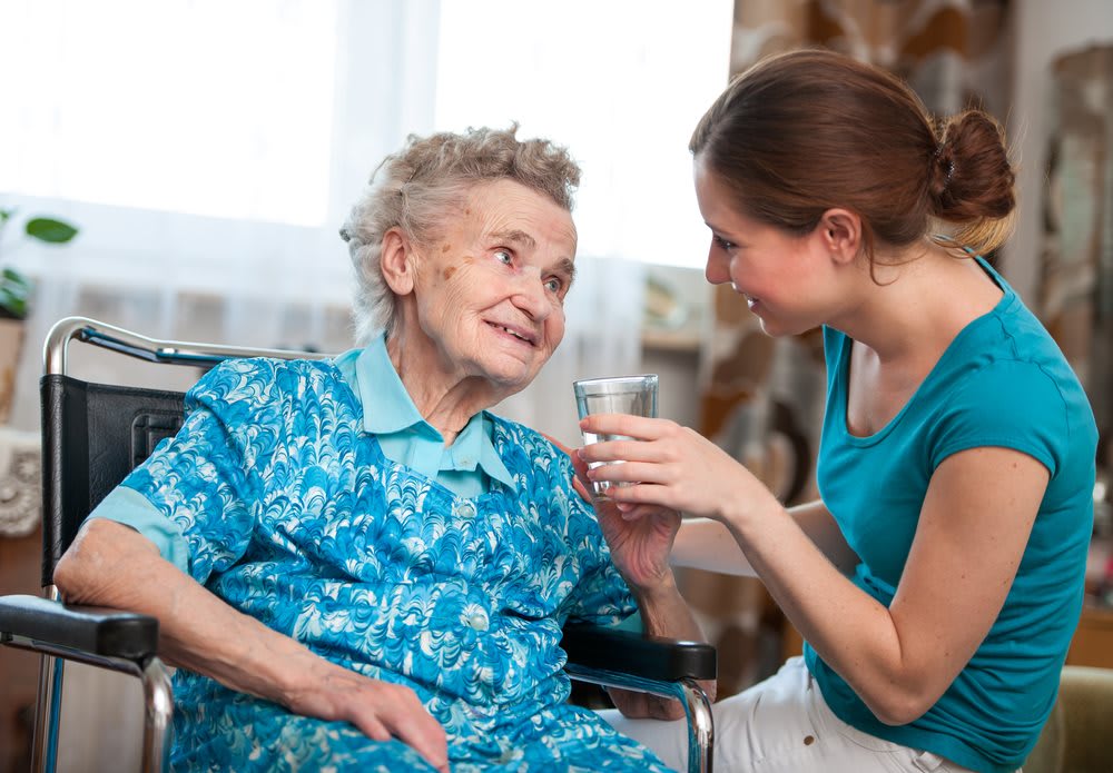 A caregiver provides assistance to an elderly woman in a wheelchair.