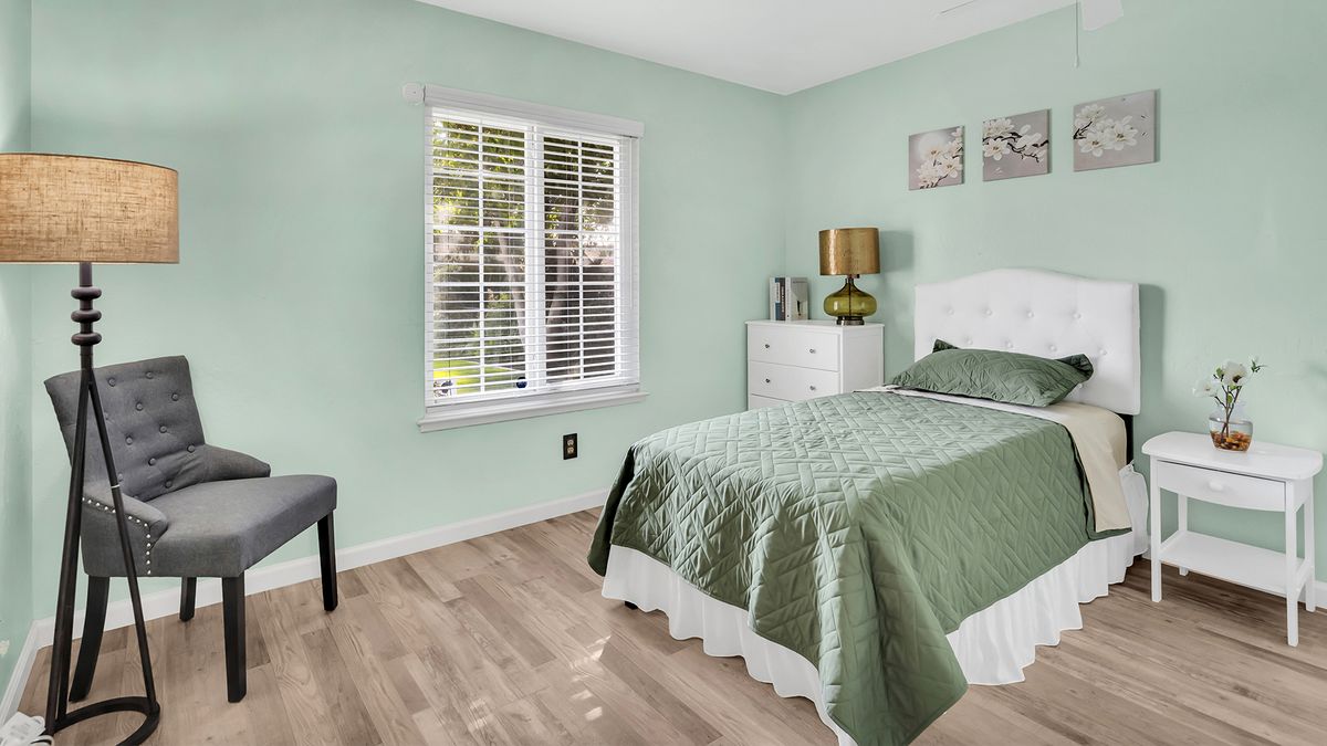 A cozy bedroom with green walls, featuring a single bed and natural light from a window with blinds.