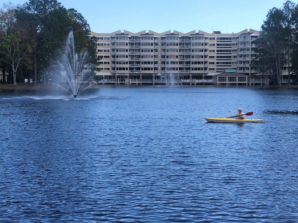 A person kayaking on a lake with fountains and apartments in the background.