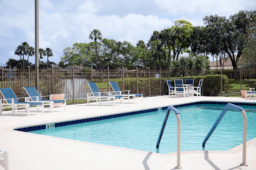 A serene outdoor swimming pool with sun loungers, surrounded by lush greenery and a clear sky.