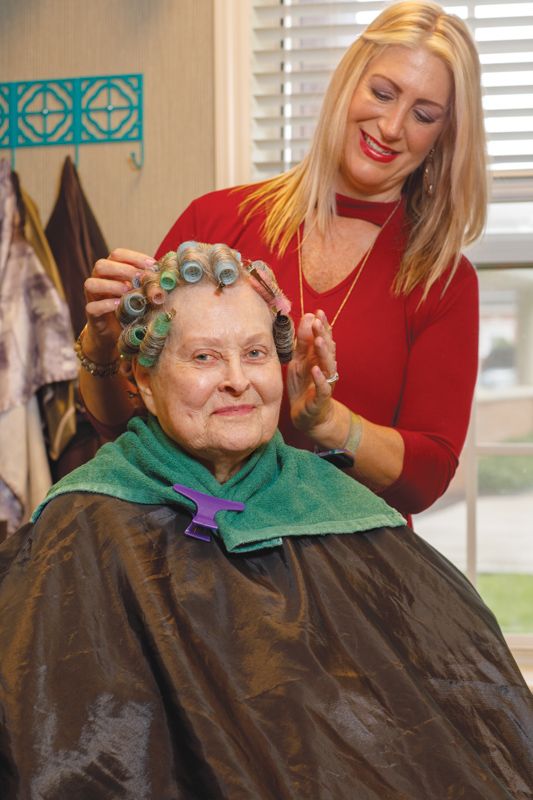 An older woman smiling while getting her hair styled with curlers at a salon.