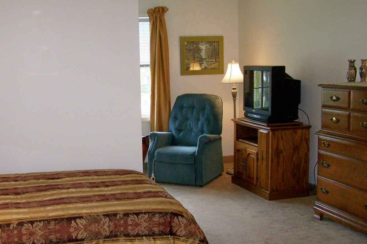 A cozy bedroom with a comfortable chair, television, and warm lighting.