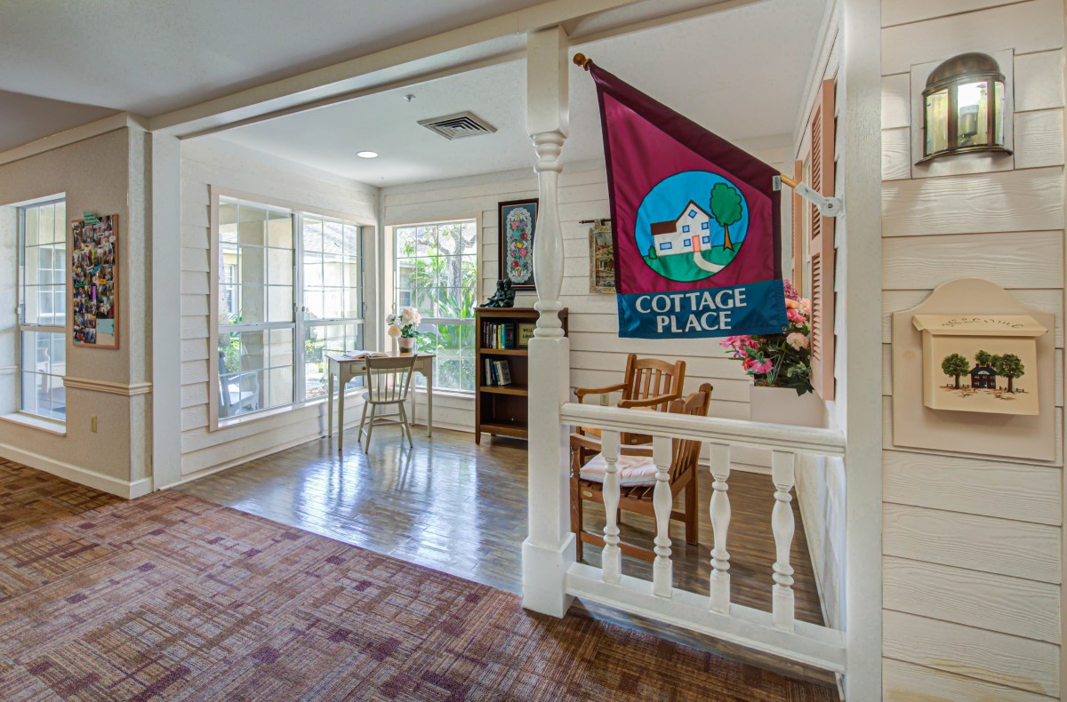 A cozy indoor space with a seating area and large windows, featuring a banner that reads 'Cottage Place'.