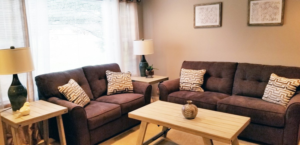 A cozy living room with dark sofas, a wooden coffee table, and a lamp by the window.