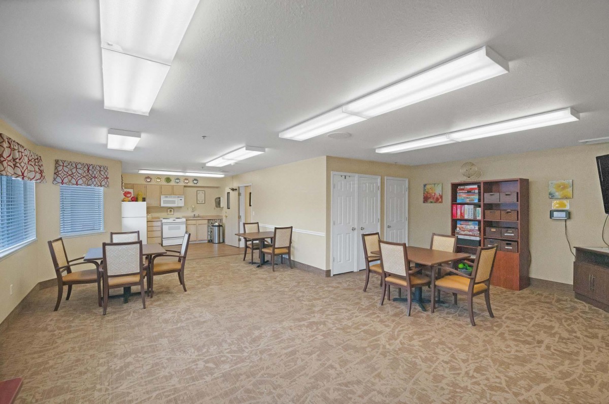 A spacious room with tables and chairs, featuring bright lighting and a small kitchen area.
