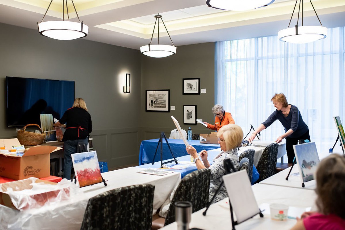 A group of people participating in an indoor painting workshop with easels set up around the room.