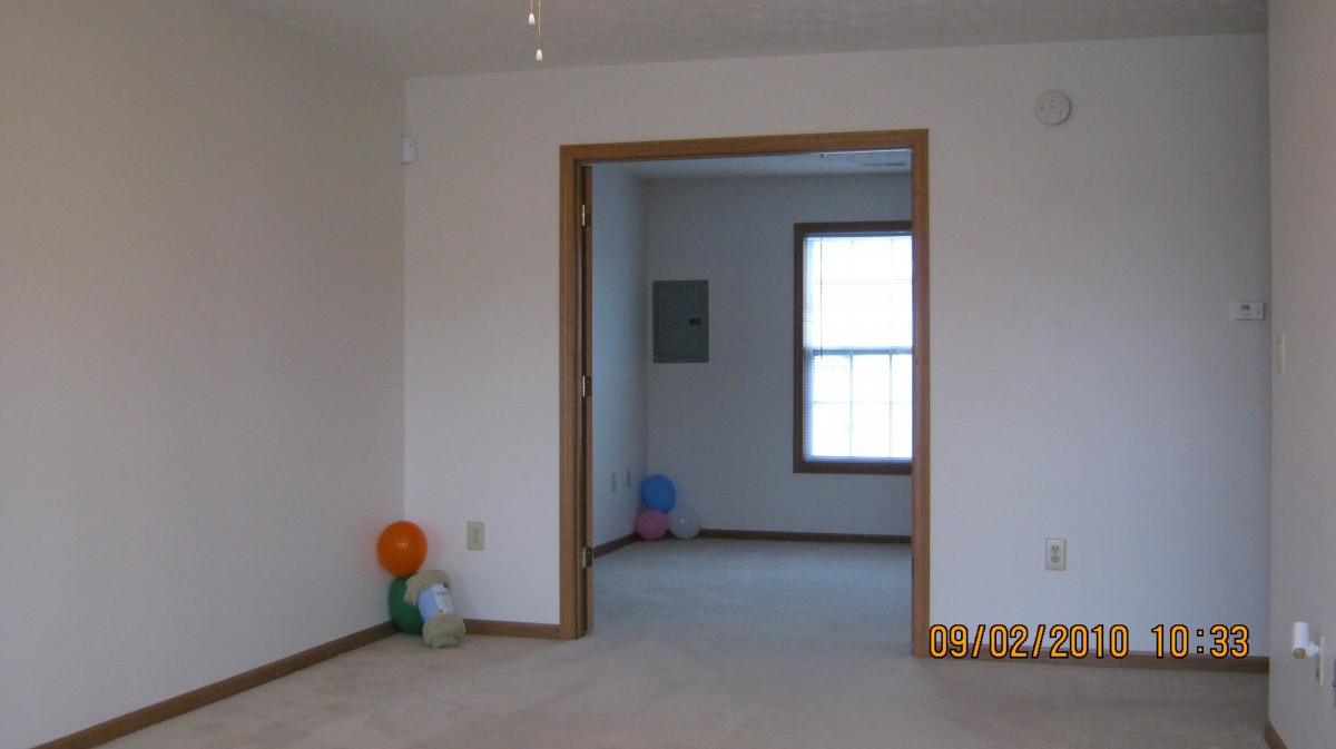 An empty room with a doorway leading to another room, featuring balloons on the floor and a window letting in natural light.