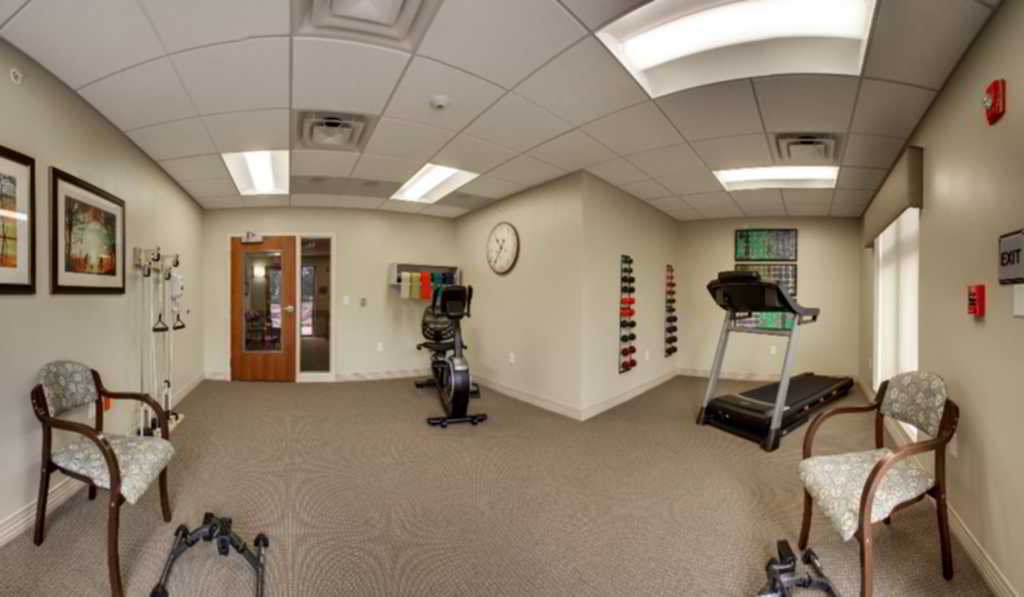A small fitness room with a treadmill, stationary bike, and weights.