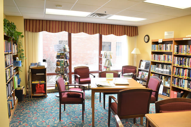 A cozy library reading room with bookshelves, table, and chairs.