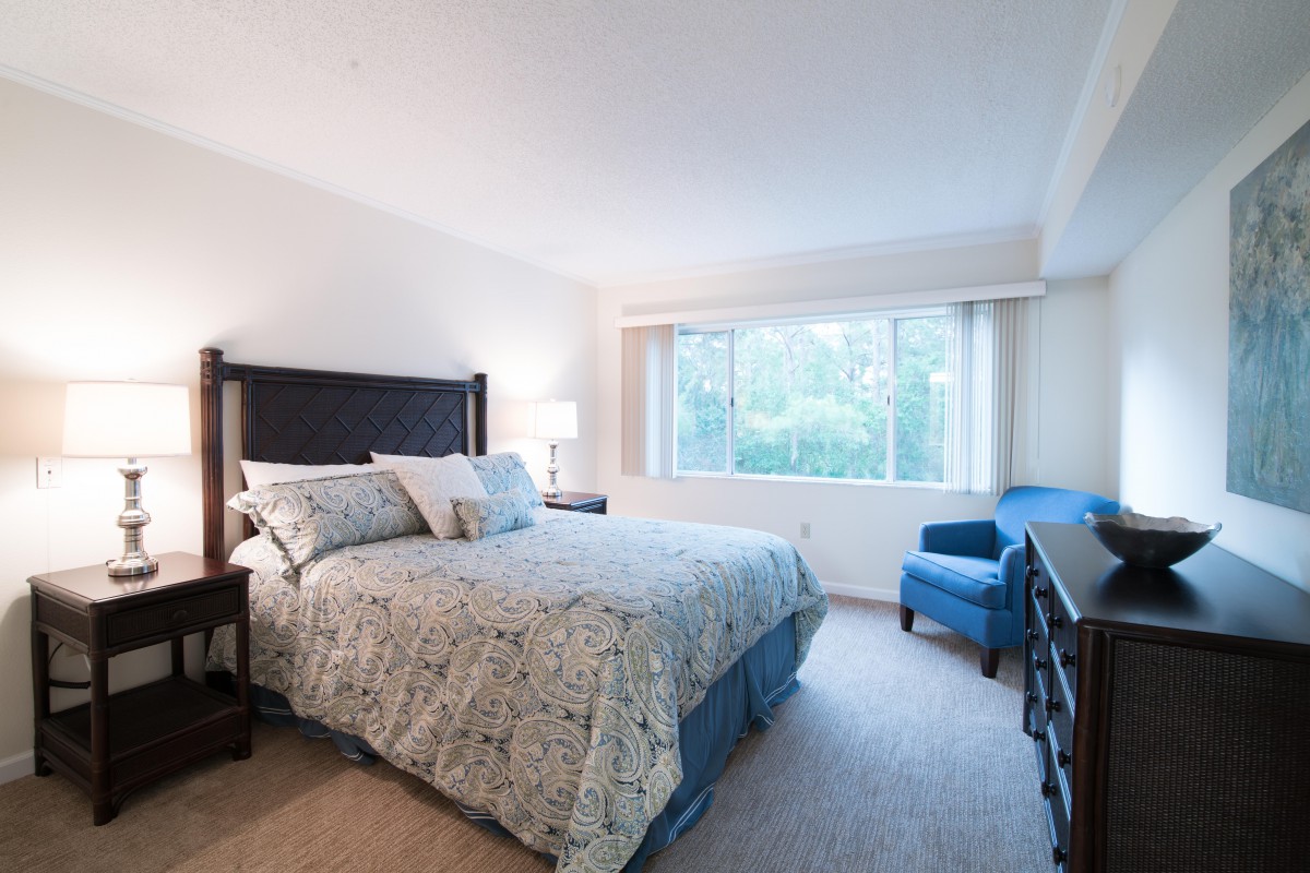 A cozy bedroom with a large window, featuring a bed and a blue armchair.