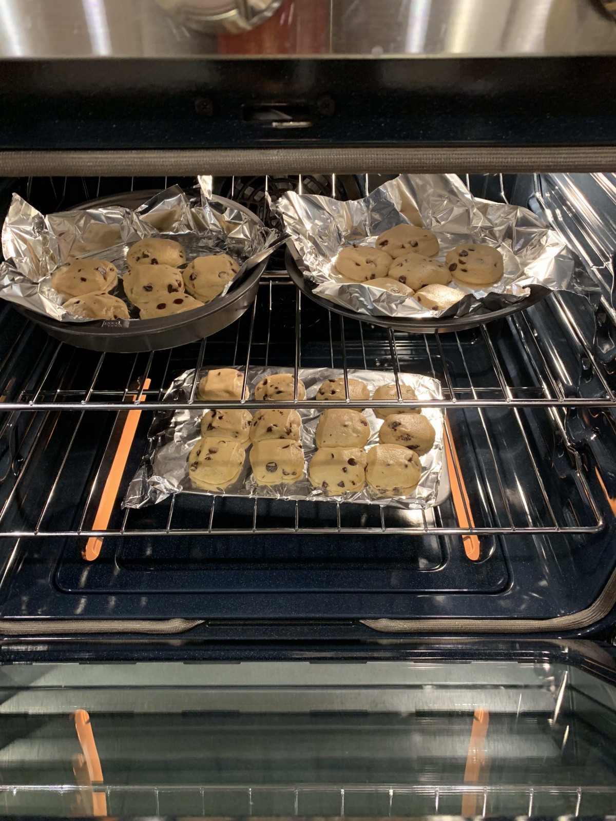 Chocolate chip cookies baking in the oven on foil-lined trays.