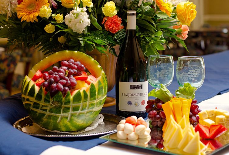 A vibrant table setting featuring a carved watermelon filled with grapes, accompanied by a wine bottle and decorative flowers.