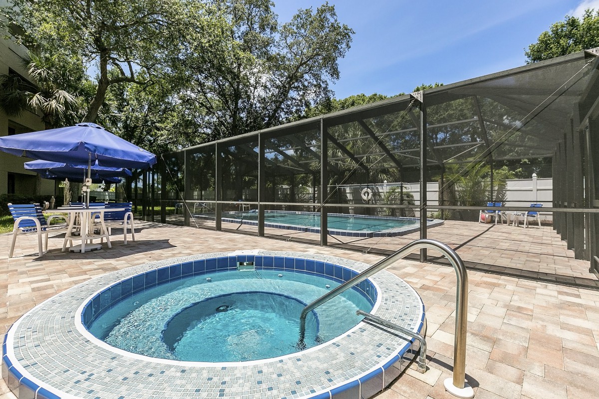 An outdoor area featuring a hot tub and a fenced pool, surrounded by trees.