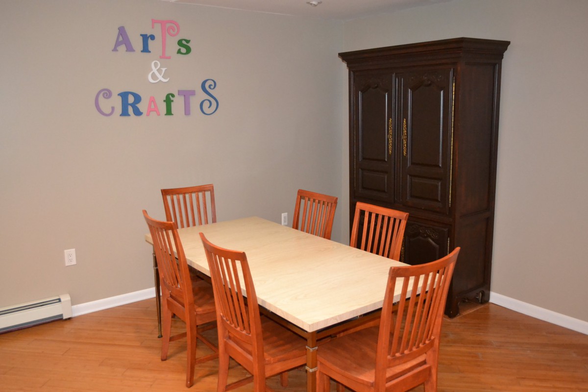 A dining room setup with a wooden table and chairs, featuring an 'Arts & Crafts' sign on the wall.