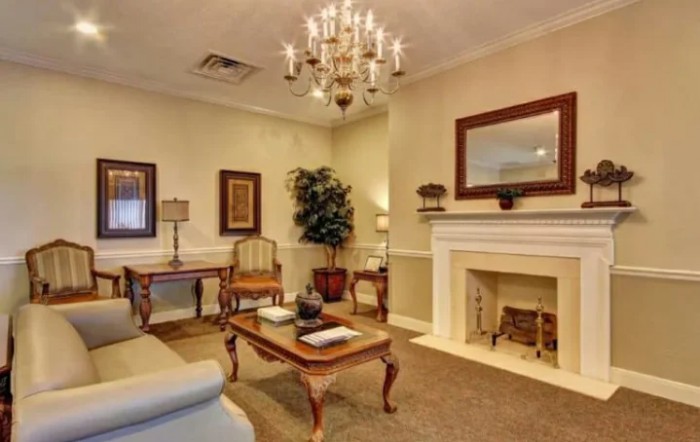 A cozy living room with a chandelier, featuring traditional furniture and a decorated fireplace.