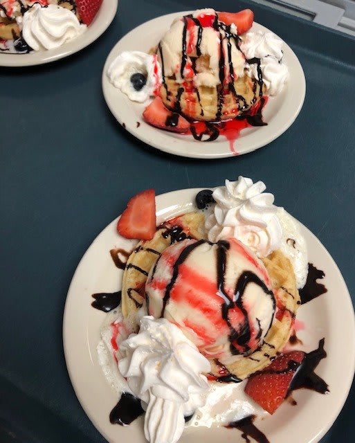 Delicious dessert featuring ice cream, strawberries, whipped cream, and chocolate sauce.