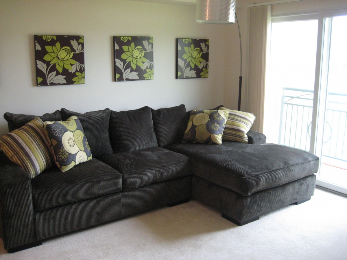 A cozy living room featuring a dark sectional sofa adorned with patterned pillows, complemented by floral wall art and a large window providing natural light.