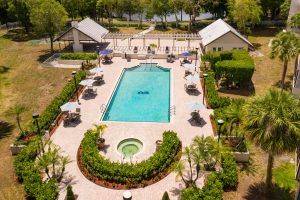 Aerial view of a landscaped swimming pool area with surrounding patio and buildings.