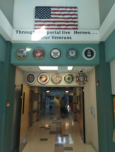 A tribute to veterans displayed at the entrance of a community center, featuring various military insignias and an American flag.