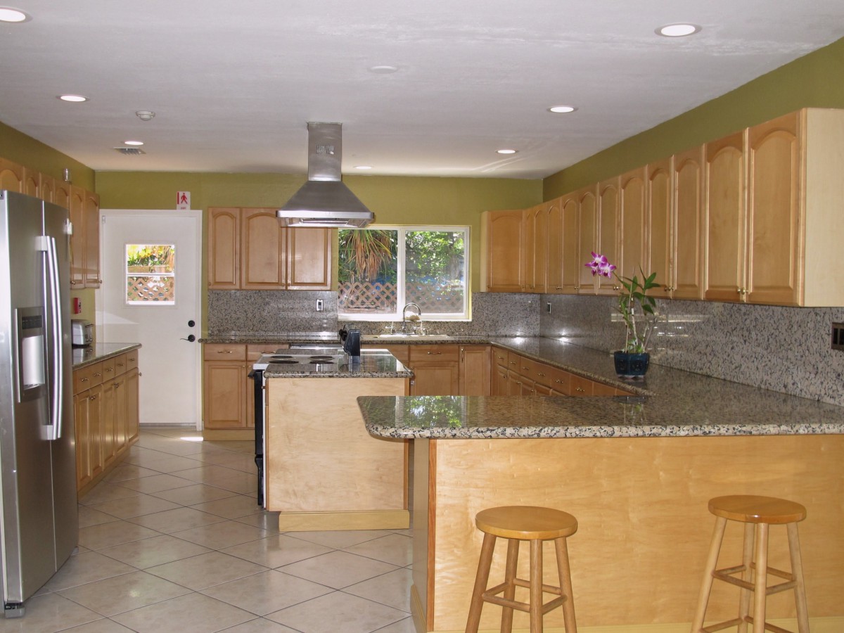 A modern kitchen with wooden cabinets and granite countertops, featuring an island with stools.