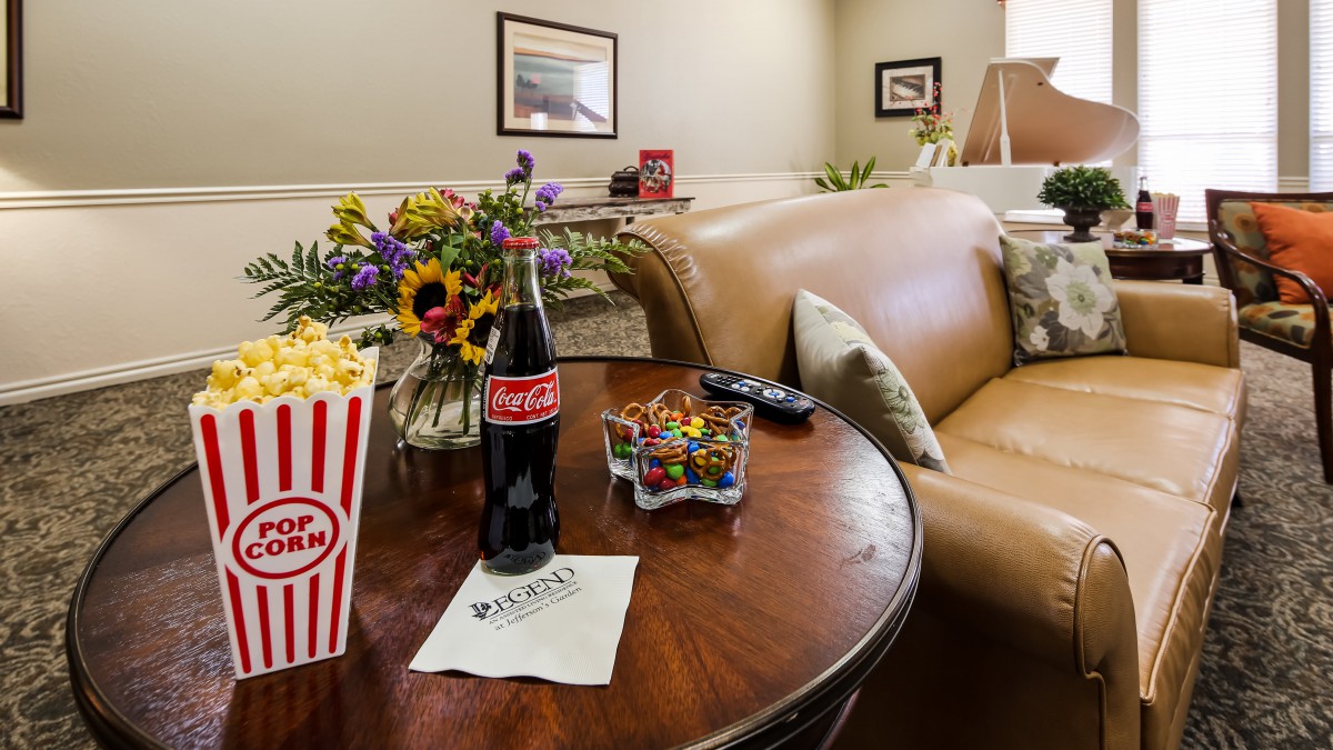 A cozy living room setup with popcorn, a Coca-Cola bottle, and a candy bowl on the table next to a comfortable sofa.