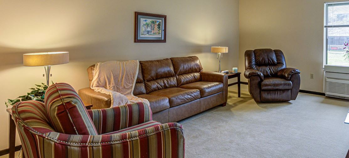 A cozy living room featuring a brown leather sofa, a striped armchair, and a standing lamp.