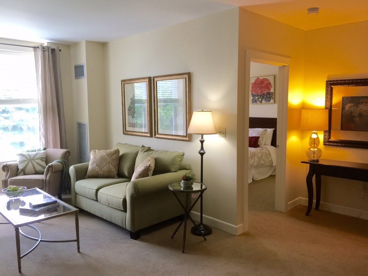 A cozy living room with elegant decor, featuring a comfortable sofa, lamps, and a view into an adjacent bedroom.
