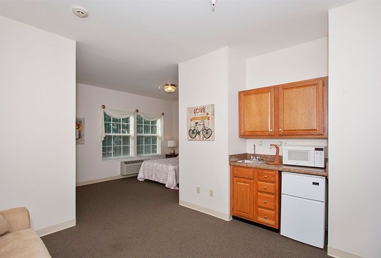 A cozy studio apartment featuring a kitchenette and bedroom area with natural lighting.
