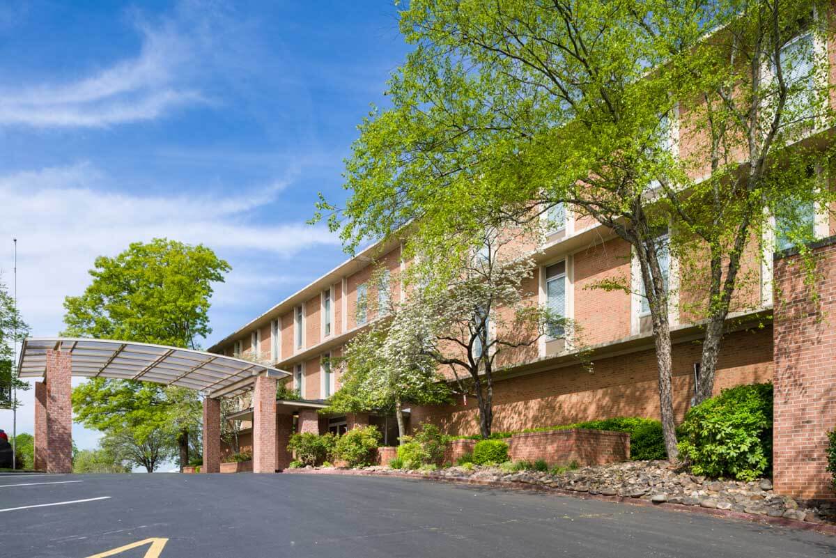 A brick hotel building surrounded by trees under a clear blue sky.