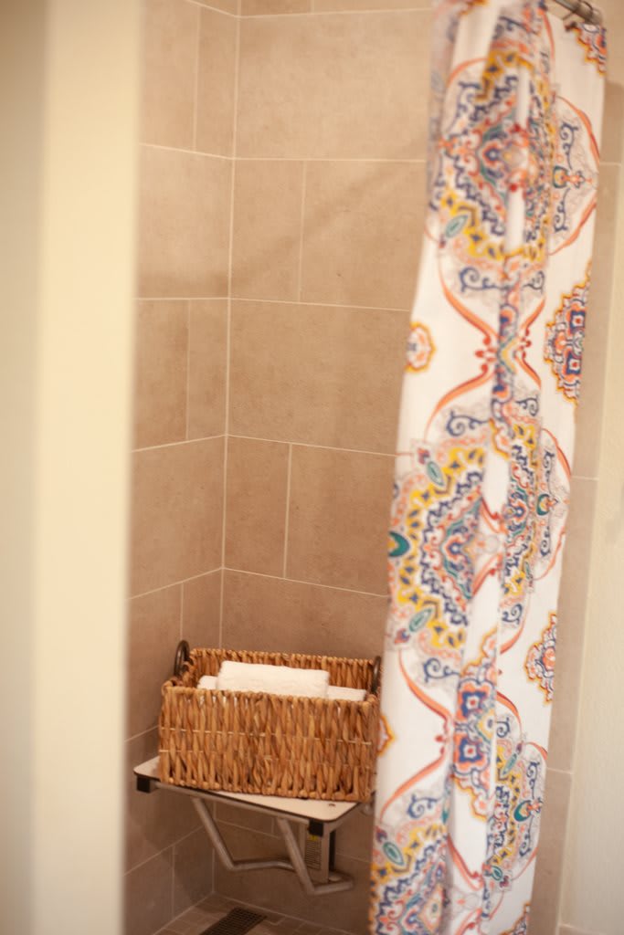 A bathroom shower area with a colorful patterned curtain and a wicker basket for storage.