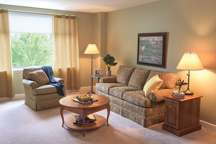 A cozy living room with a sofa, armchair, and coffee table, illuminated by warm lighting from a standing lamp.