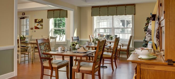 A brightly lit dining room with neatly arranged tables and chairs, featuring elegant decor and large windows letting in natural light.