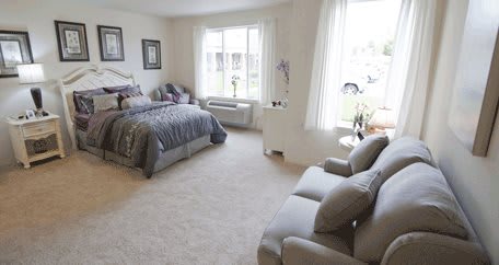 A spacious bedroom with a cozy bed, sofa, and large windows allowing natural light.