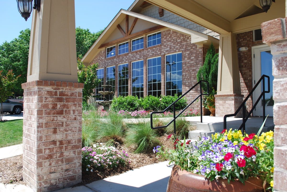 A beautifully landscaped brick building with large windows and colorful flowers in the foreground.