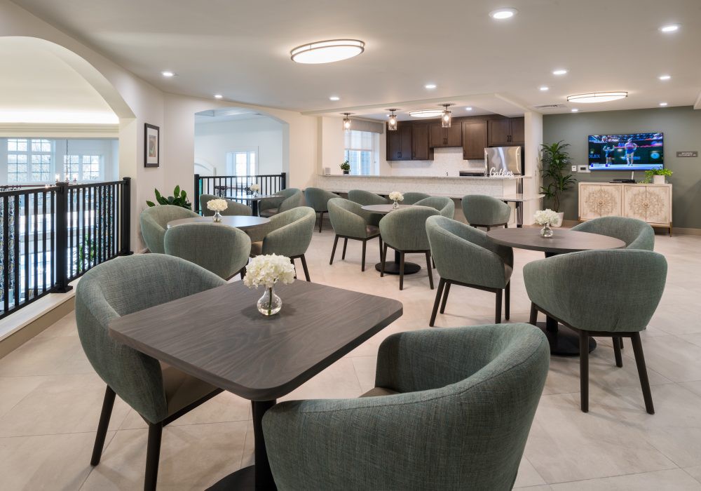 A modern dining area with several tables and chairs, adjacent to a kitchen with contemporary lighting.