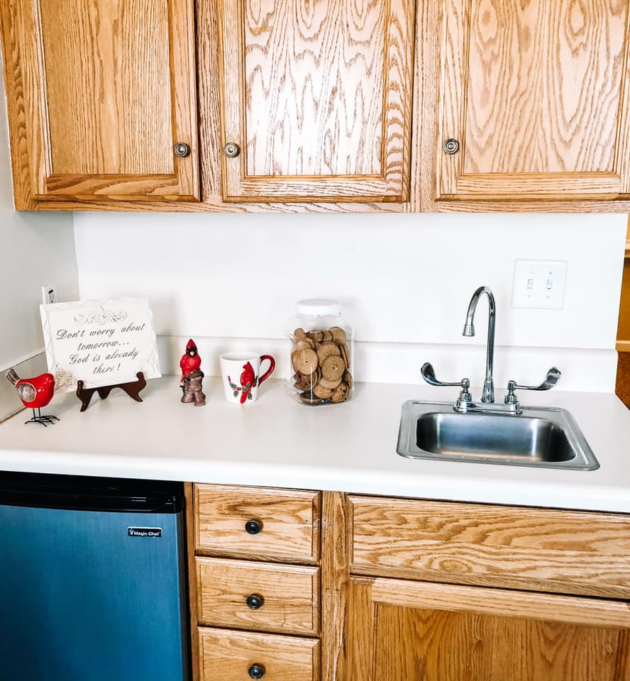 A kitchen countertop featuring wooden cabinets, a sink, decorative items, and a jar of cookies.