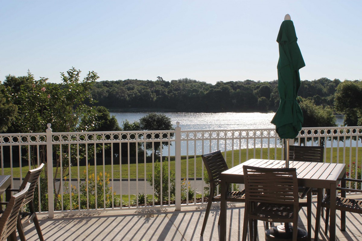 A serene lakeside view from a deck with outdoor seating and an umbrella.
