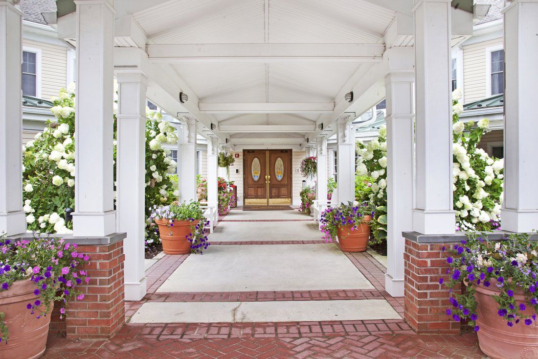 A covered entrance with columns and potted plants leading to a wooden double door.